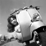 Ragazza sorridente che fa capolino dietro una Vespa.