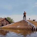 Ucraina, un uomo suona il sax sopra il tetto di una casa allagata