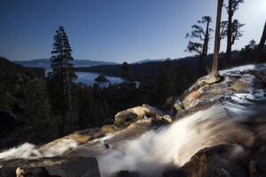 EAGLE FALLS IS ILLUMINATED AT NIGHT WITH EMERALD BAY AND LAKE TAHOE IN THE BACKGROUND IN LAKE TAHOE