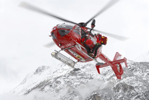 AN EMERGENCY DOCTOR, PATIENT AND PARAMEDIC ARE HANGING OUTSIDE A HELICOPTER DURING A RESCUE MISSION FOR AN INJURED SKI MOUNTAINEER.