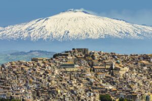 HILL TOWN WITH BACKDROP OF SNOWY VOLCANO MOUNT ETNA