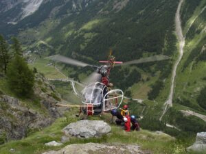 MOUNTAIN RESCUE PERSONNEL IS CAREFULLY LOADING INTO A HOVERING HELICOPTER.