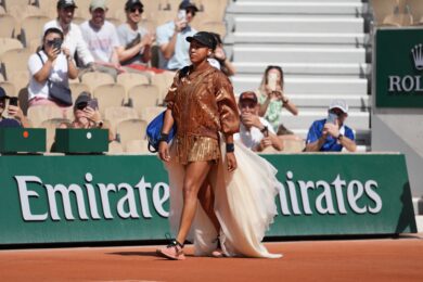 Naomi Osaka entra in campo sfilando come una modella. Fasciata in un bomber che sembra richiamare la terra rossa del Roland Garros e con uno strascico a cingerle i fianchi, l'atleta raggiunge la propria metà campo prima di affrontare la croata Donna Vekić. (AP Photo/Thibault Camus)