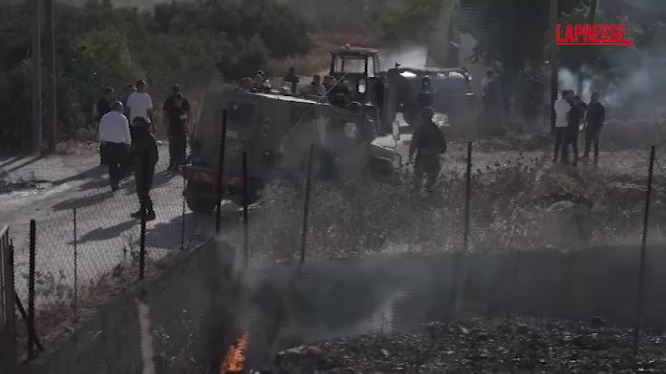 Strada in zona collinare palestinese, veicoli militari, abitazioni danneggiate, tensione tra forze armate e civili