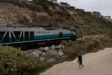 Le spiagge della California si stanno progressivamente restringendo . Un surfista cammina lungo North Beach mentre un treno della Metrolink viaggia lungo la costa a San Clemente, in California (Foto AP/Jae C. Hong)